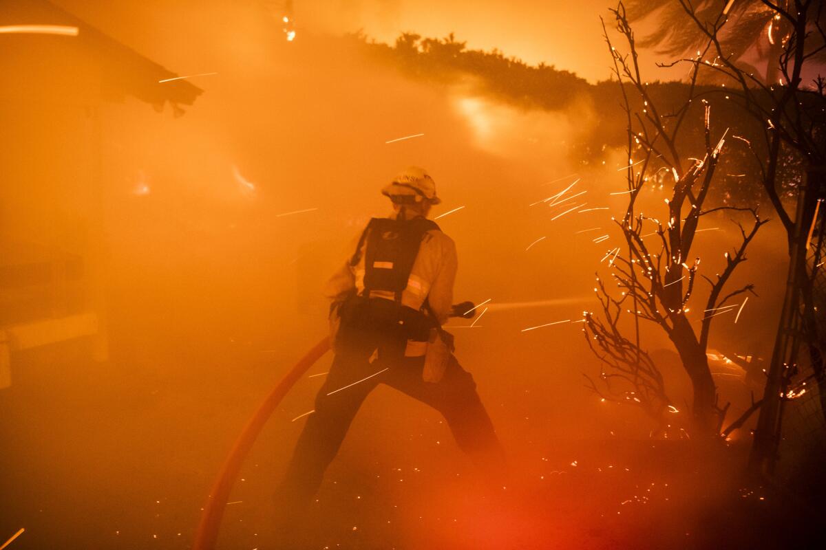 A firefighter extinguishes brush threatening a home on Quinta Vista Drive and East Hillcrest Road in Thousand Oaks from the Woolsey Fire.