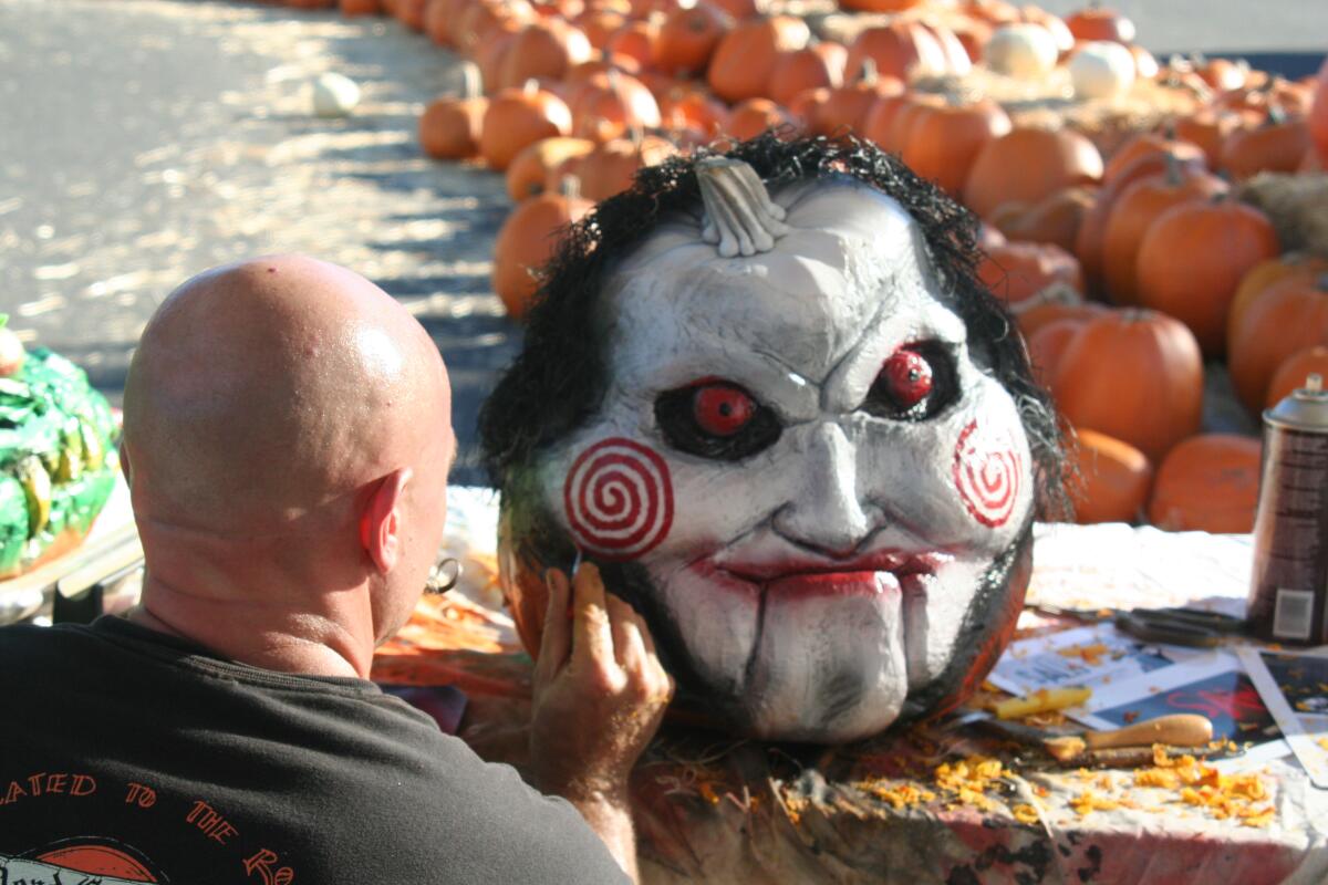 A bald man paints a large pumpkin to look like a goblin.