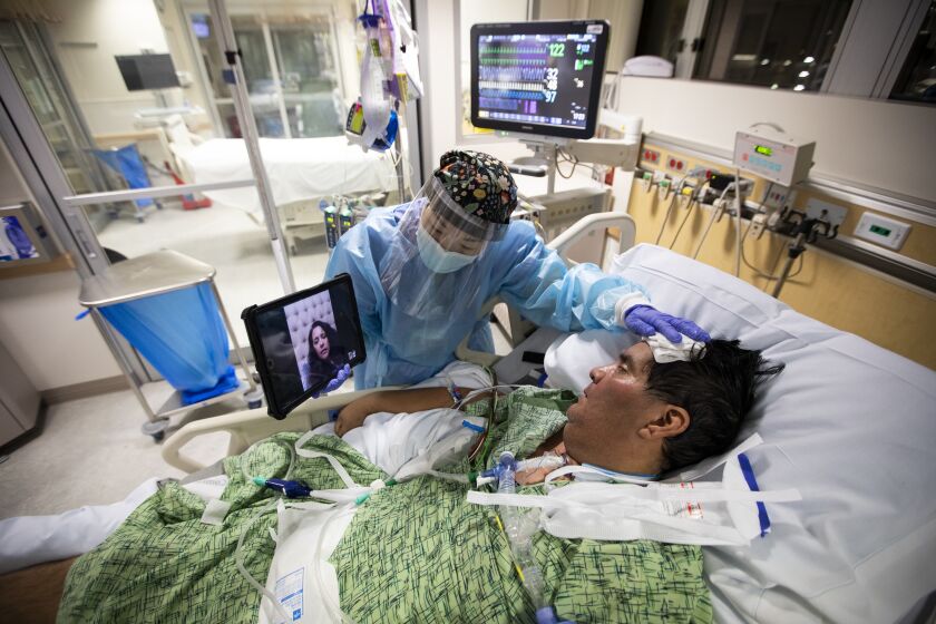 Kat Yi holds an iPad up to Eduardo Rojas, 50, so that his wife can see him inside the ICU 