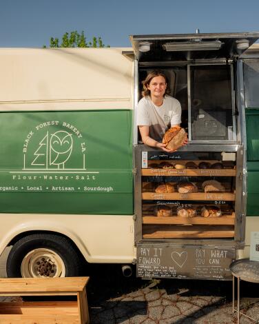 A person leans out of a van holding a fresh loaf of bread