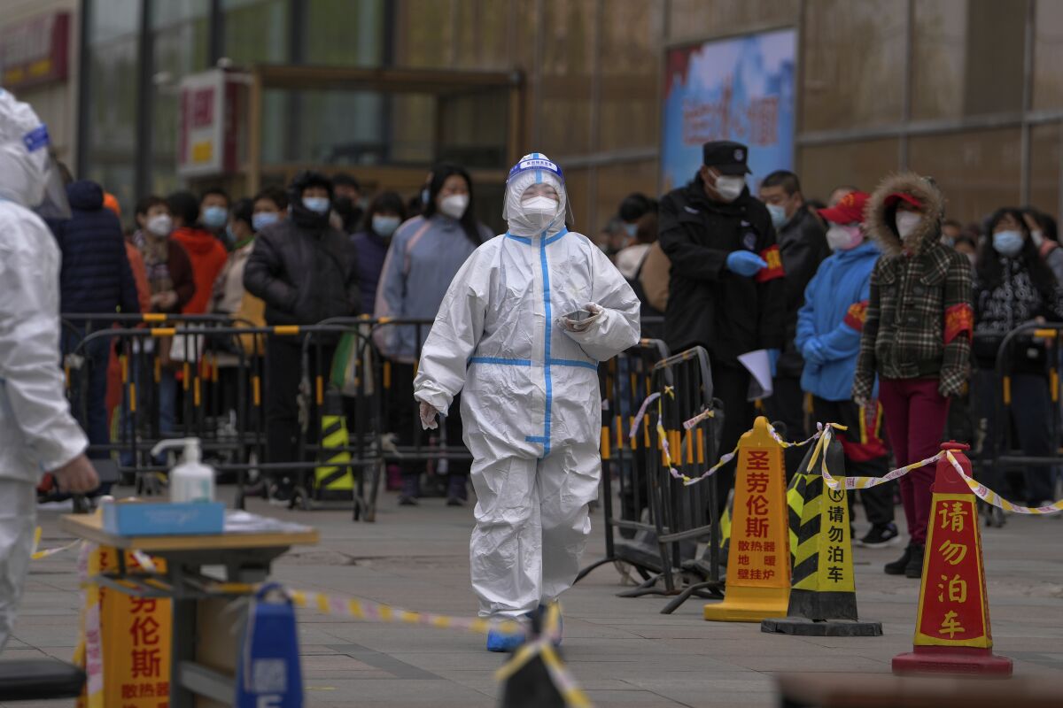 Health worker in full-body protective suit walks next to a line of people
