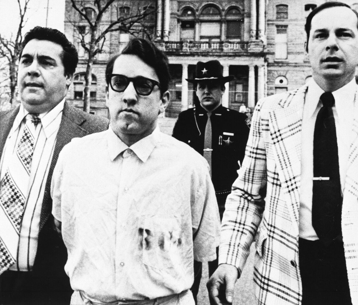 FILE - Mass murderer James Ruppert, center, is taken back to jail after his arraignment in Hamilton, Ohio, on eleven counts of aggravated murder, April 8, 1975. Ruppert, 88, who was serving a life sentence for the shooting deaths of 11 family members — including eight children — died Saturday, June 4, 2022, at the prison system’s Franklin Medical Center in Columbus. (AP Photo/Brian Horton, File)