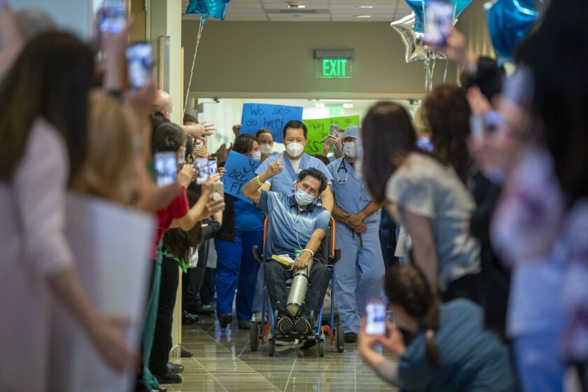ORANGE, CA -- TUESDAY, MAY 5, 2020: Armando Mendoza, 53, of Anaheim, who was the hospital's second-ever COVID-19 patient, spent 45 days at St. Joseph Hospital, the longest local stint of any COVID-19 patients, celebrates with gratitude to God, all his health-care professionals (his nurse, Puynh Nguyen pushes his wheel chair and his doctor, Dr. Jooby Babu to his right) and his family and supporters as he is released to his awaiting family with applause and salutes from hospital workers in Orange, CA, on May 5, 2020. Mendoza was healthy and had no underlying health conditions when he contracted the virus. (Allen J. Schaben / Los Angeles Times)