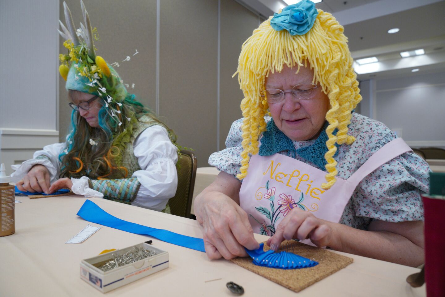 Karen Wallach (left) dressed as the Woodland Wanderer and Susan Farnham dressed as Nellie Oleson learn to sew a ribbon cockades at the costume workshop during Costume-Con this past weekend in Mission Valley.