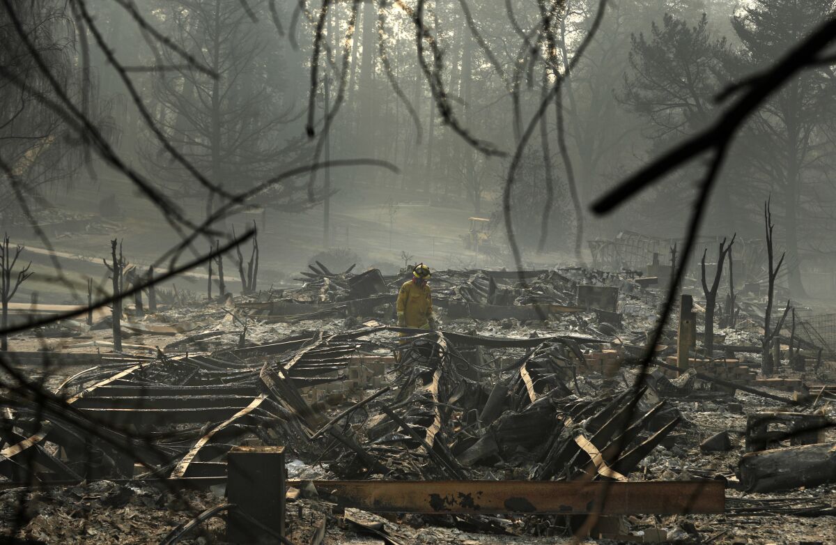 FILE -A firefighter searches for human remains in a trailer park destroyed in the Camp Fire, Friday, Nov. 16, 2018, in Paradise, Calif. A lobbyist seeking a $1.5-billion state loan to help tens of thousands of victims of devastating California wildfires is leaving his job amid a sexual harassment scandal. The PG&E Fire Victim Trust reported Wednesday, April 20, 2022 that Patrick McCallum and the trust “have agreed to part ways." (AP Photo/John Locher, File)