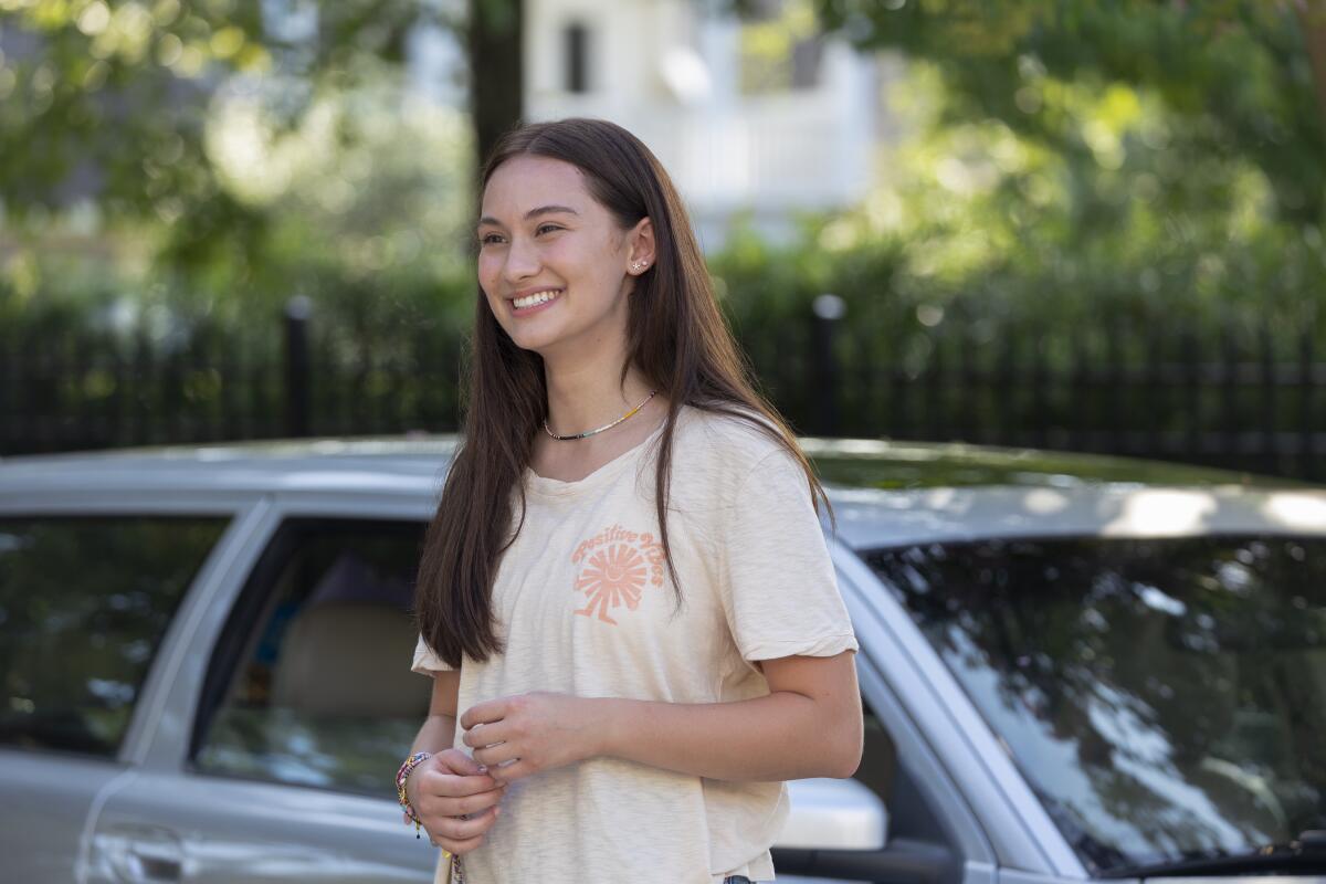 A teenage girl standing by a car smiling