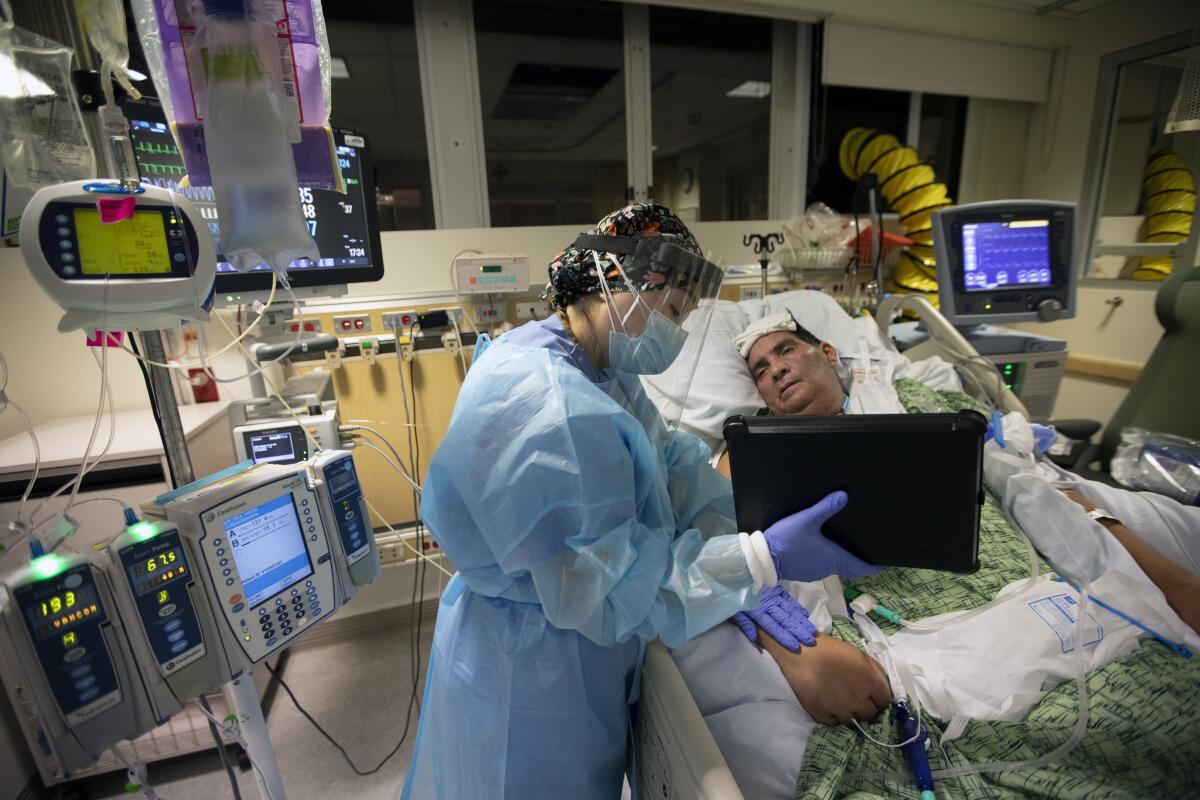 Nurse Kat Yi holds an iPad up to Eduardo Rojas, 50, so that his wife can talk to him. 