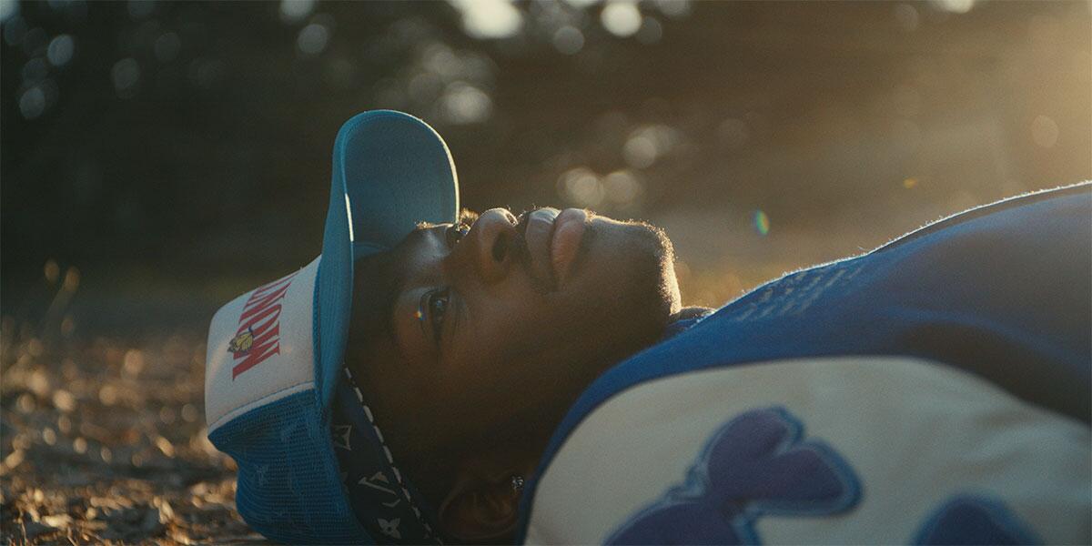 Lil Nas X lying on the ground in a blue-and-white hat and sweatshirt.