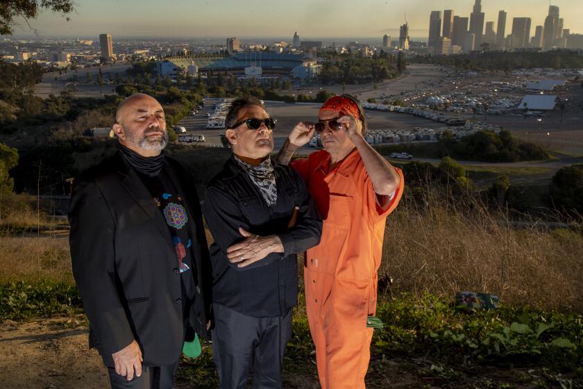 LOS ANGELES, CA - FEBRUARY 24, 2021: Members of the Latin comic group Culture Clash at Elysian Park overlooking Dodger Stadium and the LA skyline on February 24, 2021 in Los Angeles, California. The performance troupe of Herbert Siguenza, left, Ric Salinas, middle and Richard Montoya, right, are also contributing performers at the CTG.(Gina Ferazzi / Los Angeles Times)