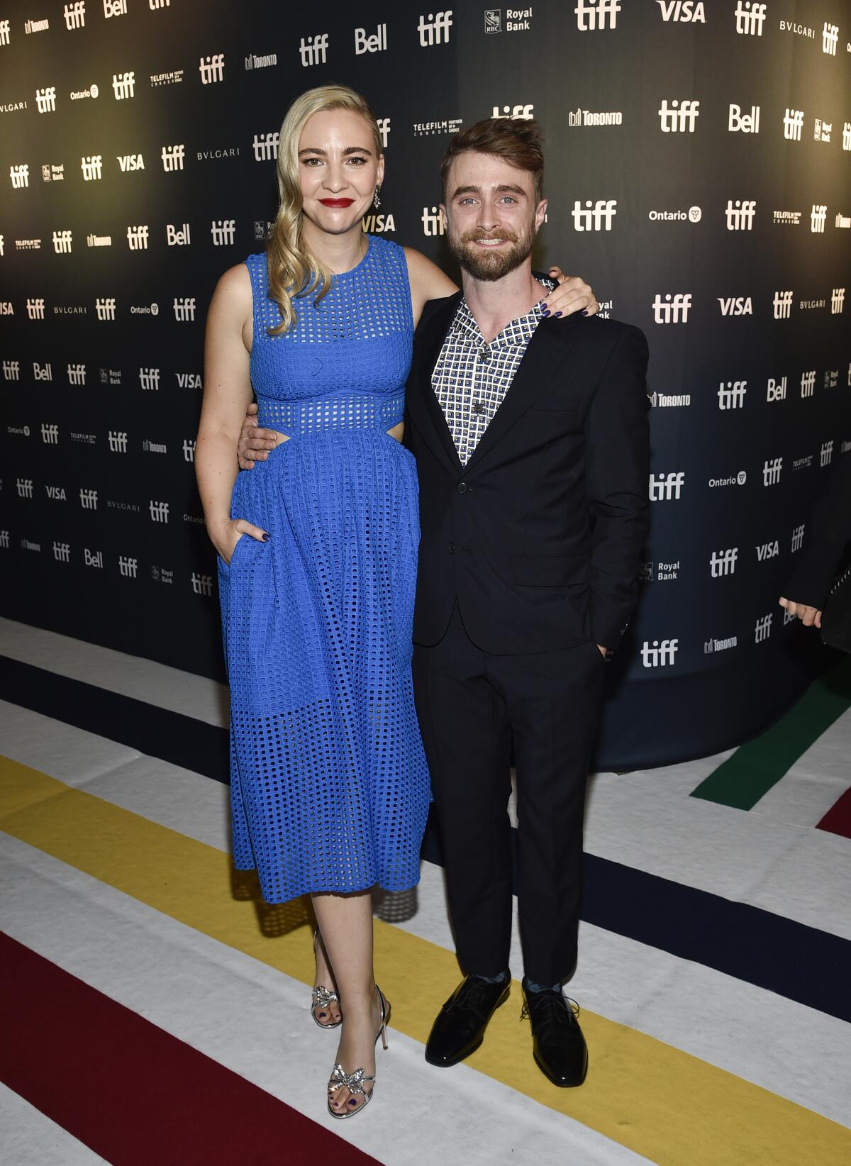Erin Darke in a bright blue gown standing next to Daniel Radcliffe in a checkered shirt and black suit