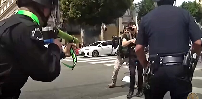 A police officer points a weapon at a protester
