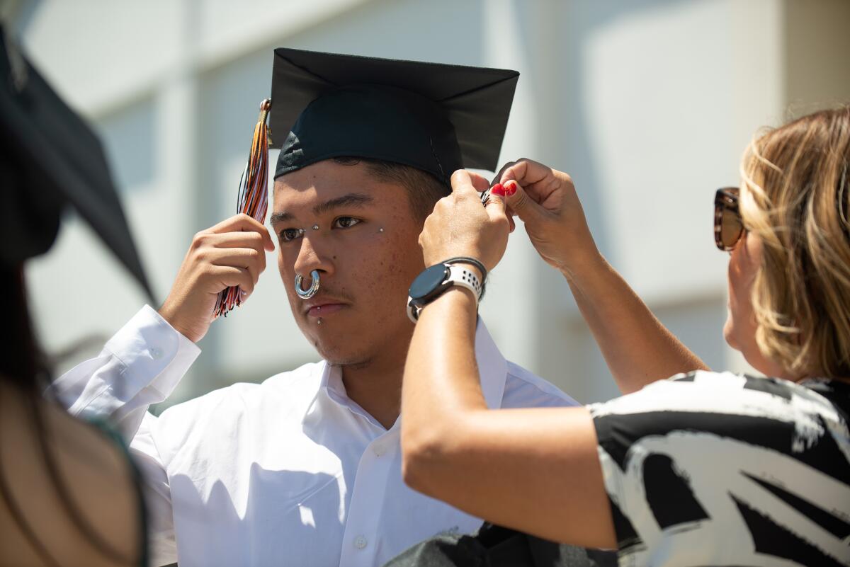 Andre Contreras holds his tassel while teacher Christy Montes adjusts his cap before the Los Amigos High graduation ceremony.