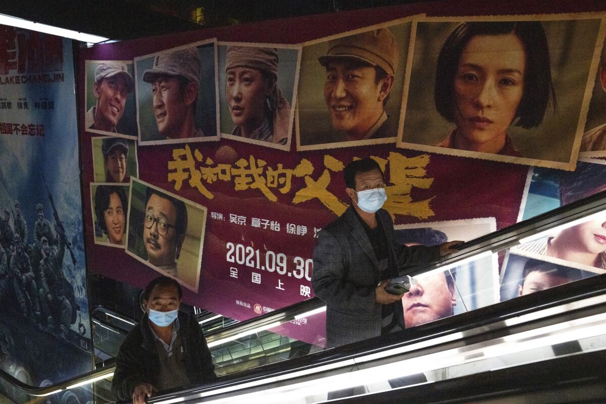 Men wearing masks pass by an advertisement for the patriotic movie "My People, My Parents" at a cinema in Beijing, China, Friday, Oct. 8, 2021. China saw a major dip in travel over the past week's National Day vacation. People staying home appeared to have chosen the cinema instead, with a patriotic Korean War film taking in more than 3.45 billion yuan ($535 million) at the box office. (AP Photo/Ng Han Guan)