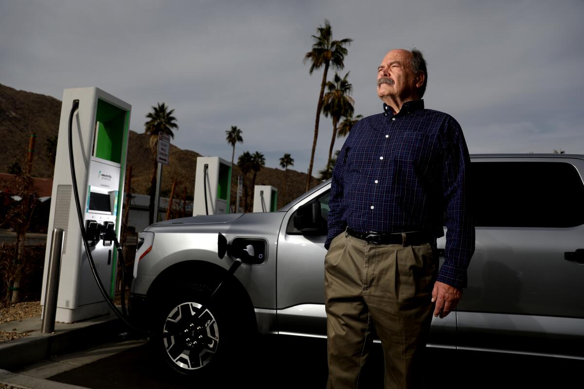 A man stands in front of a 2023 Ford F-150 Lightning electric pickup at an EV charging station