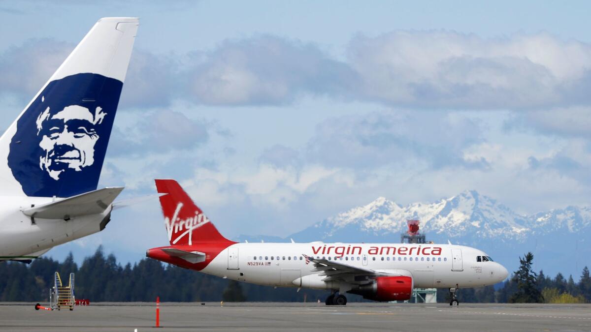 A Virgin America plane taxis past an Alaska Airlines plane at Seattle-Tacoma International Airport.