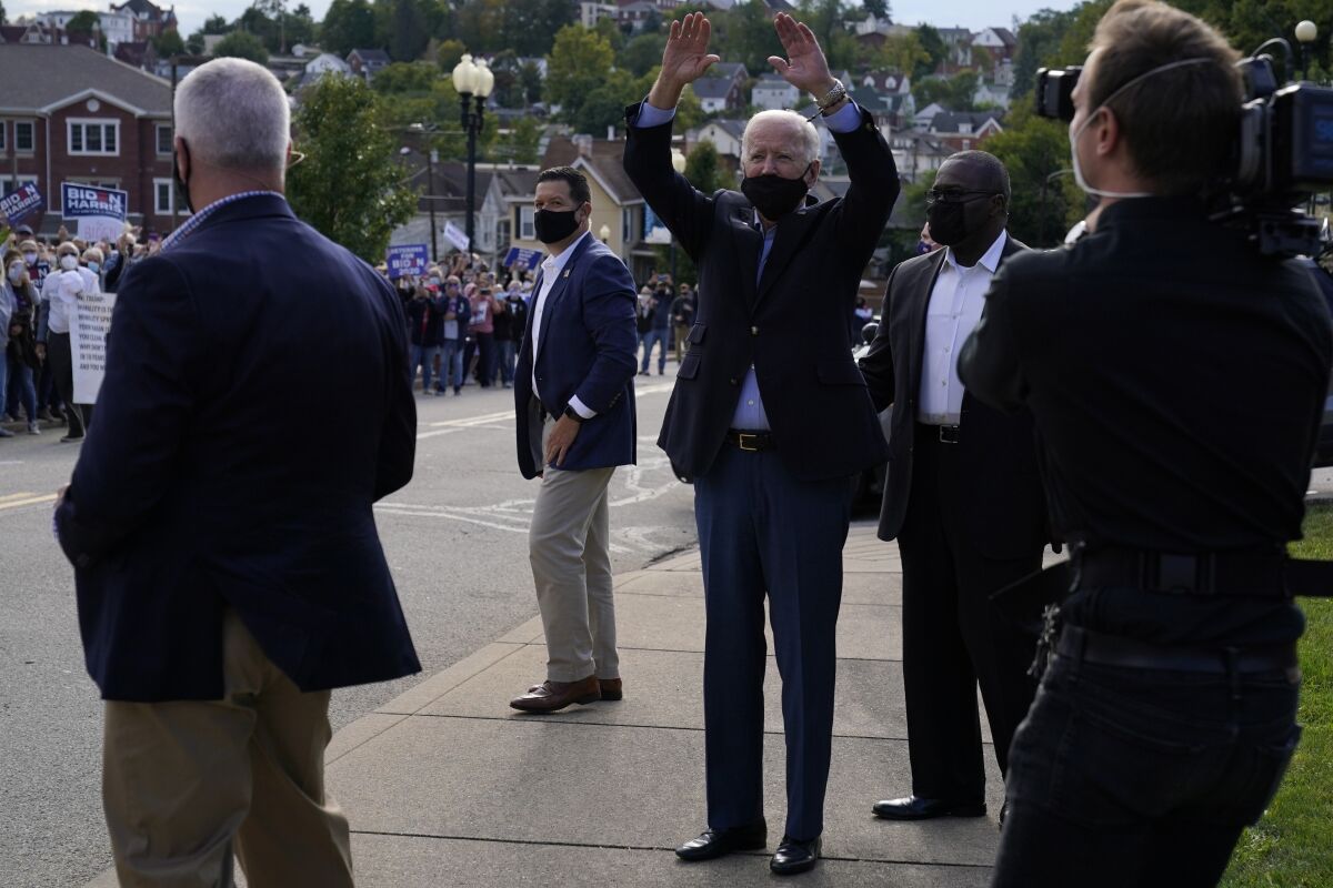 Joe Biden, wearing a mask, raises both arms to wave to supporters