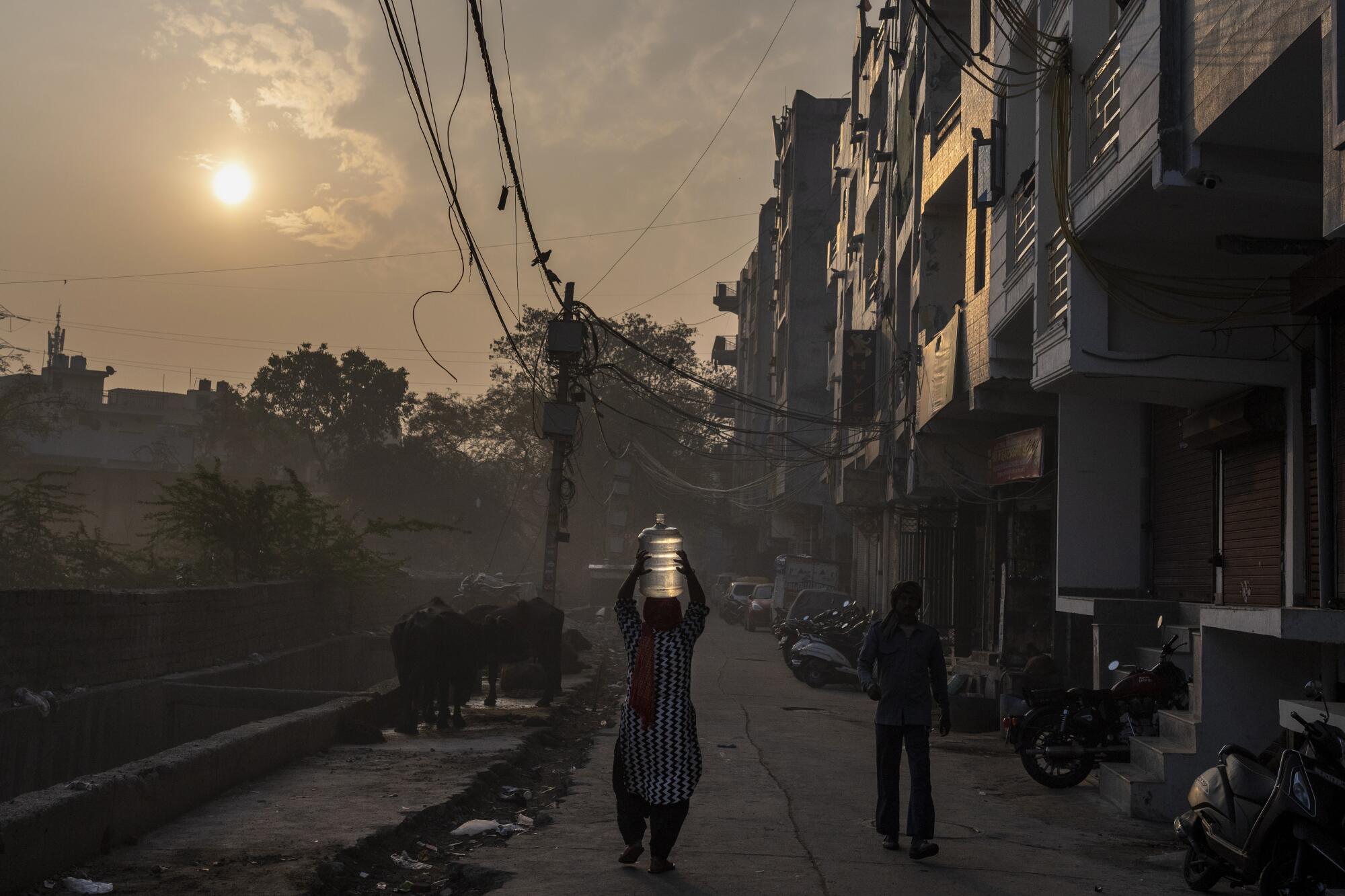 A woman carries a jug on her head in a residential area of India.