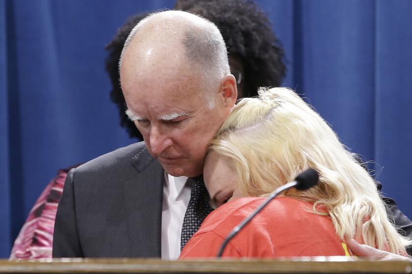 Gov. Jerry Brown is hugged by Holly Dias, a Burger King employee who praised Brown's announcement of proposed legislation to increase the state's minimum wage to $15 per hour by 2022, during a news conference in Sacramento on Monday.