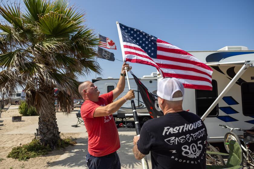 Huntington Beach, CA - May 22: Dan Steele, left, of Lake Havasu City, Arizona, and Scott Bickelhaupt, of Temecula put up their flags while setting up their campground during the Memorial Day weekend getaway at Bolsa Chica State Beach in Huntington Beach Wednesday, May 22, 2024. (Allen J. Schaben / Los Angeles Times)