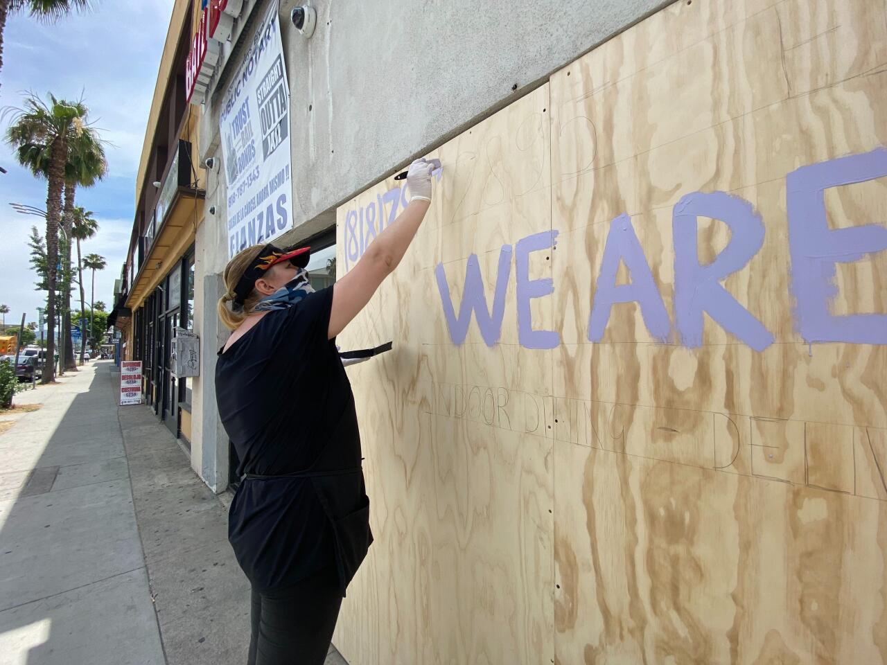 Anastasia Azaryan paints a sign on her boarded-up restaurant in Van Nuys