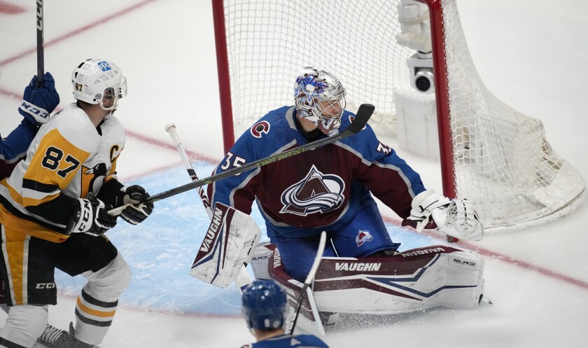 Pittsburgh Penguins center Sidney Crosby, left, puts a shot on Colorado Avalanche goaltender Darcy Kuemper in the first period of an NHL hockey game Saturday, April 2, 2022, in Denver. (AP Photo/David Zalubowski)