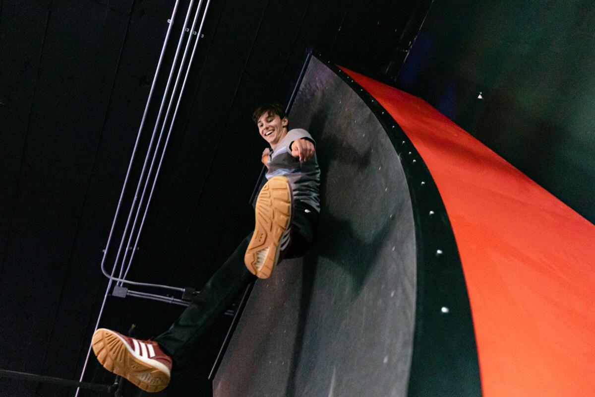 A young man hangs off the edge of a warped wall.