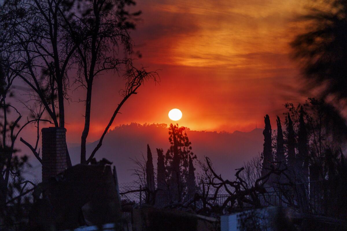 A haze of orange smoke fills the landscape at dusk as a house burns in the foreground during the Eaton Fire on January 8.