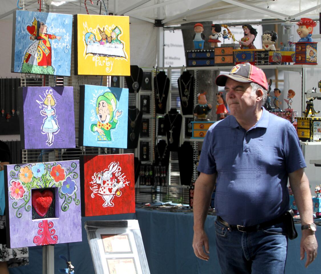 A man walks past artwork from the Yuneek booth at the Downtown Burbank Arts Festival, on San Fernando Rd., in Burbank on Saturday, April 16, 2016.