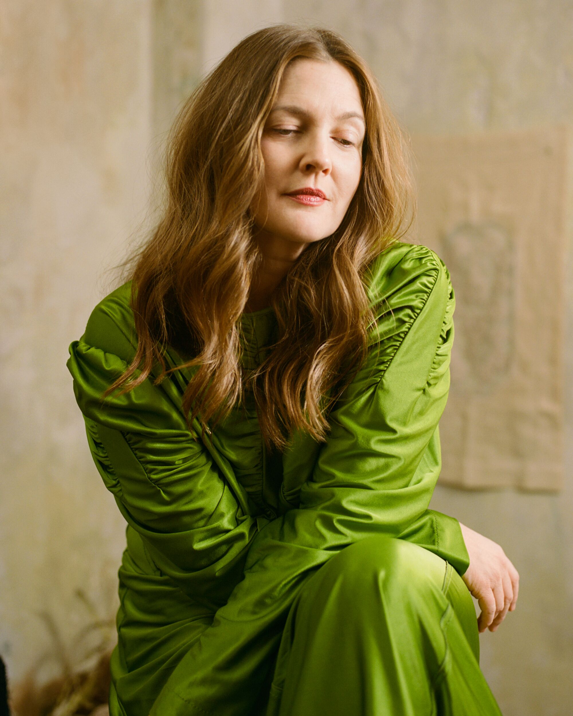 A seated Drew Barrymore, dressed in green, looks pensive.