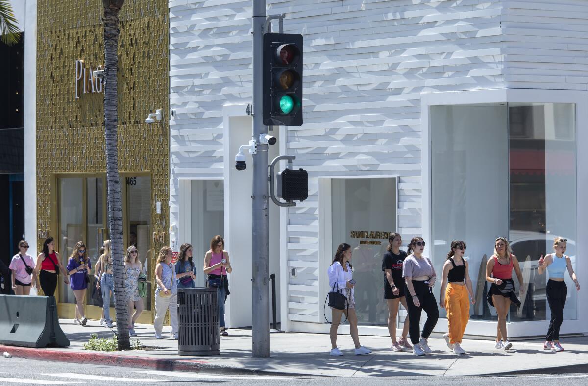 Security cameras are attached  below a traffic signal as pedestrians stroll Rodeo Drive