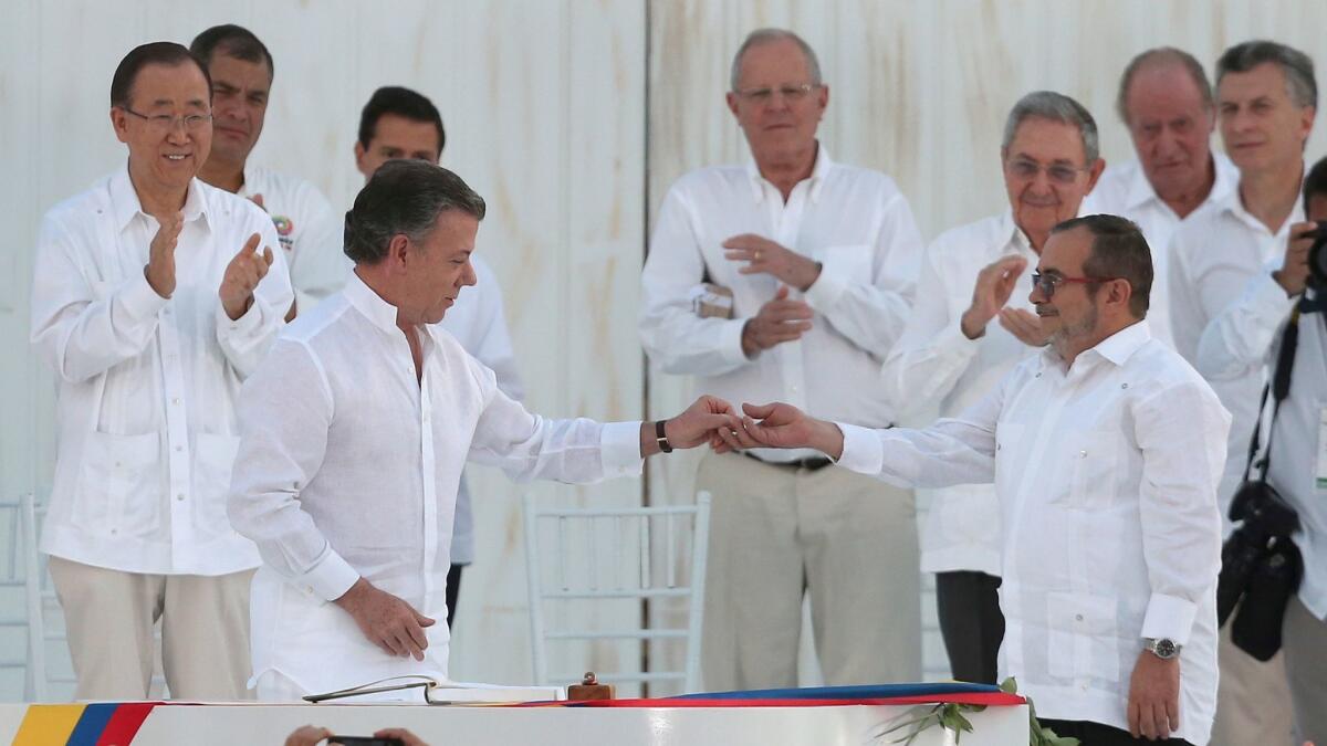 Colombia's President Juan Manuel Santos, front left, gives a peace pin to the top commander of the Revolutionary Armed Forces of Colombia, or FARC, Rodrigo Londono, on Sept. 26.