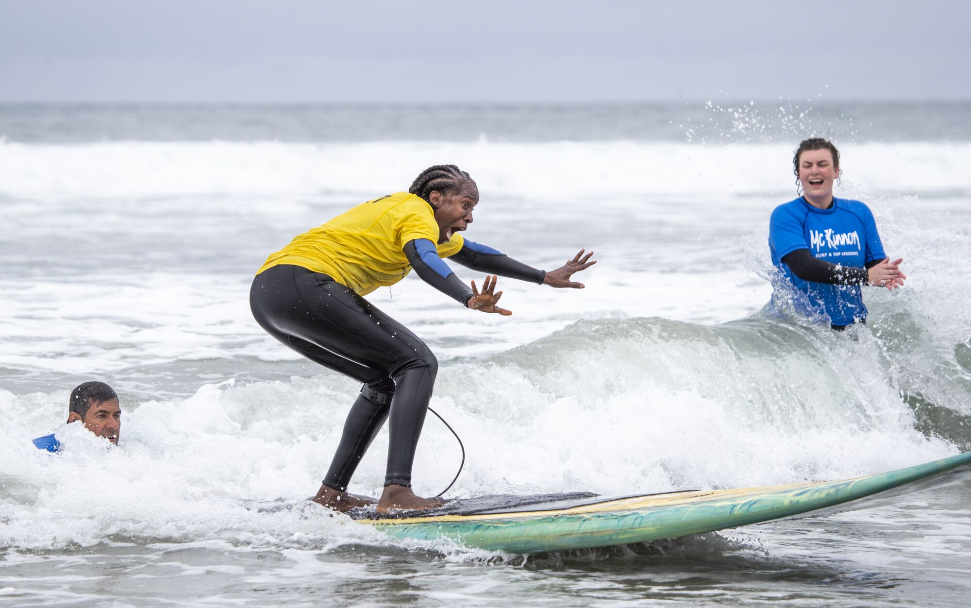 Surf coaches assist and cheer on Danielle Forbes as she rides her first wave during a surfing lesson.