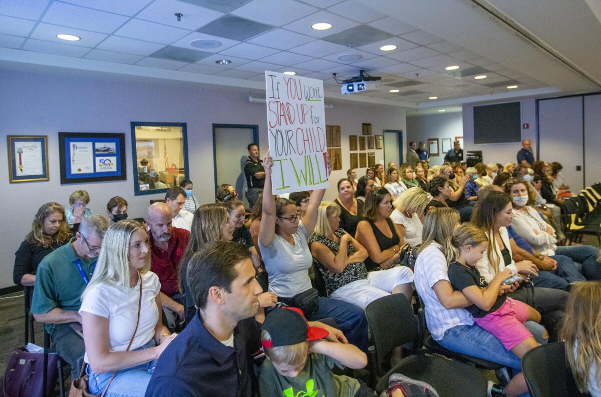 Nirina Harper holds up a sign during a Newport-Mesa Unified School District board meeting on Tuesday, Aug. 17.