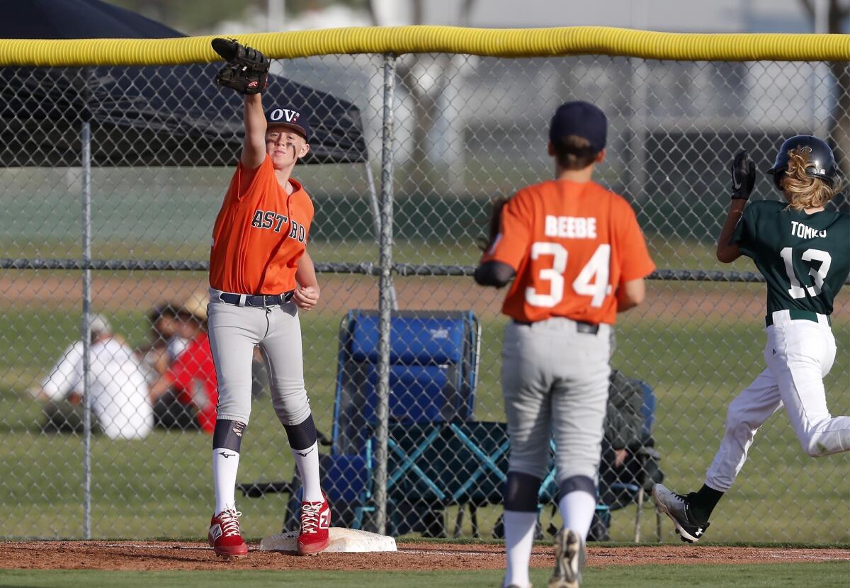 Ocean View Little League's Jack Gollinger, left, secures an out at first base against Costa Mesa American's Brady Tomko, right, in a District 62 Tournament of Champions Major Division quarterfinal game on Tuesday at Costa Mesa American Little League.