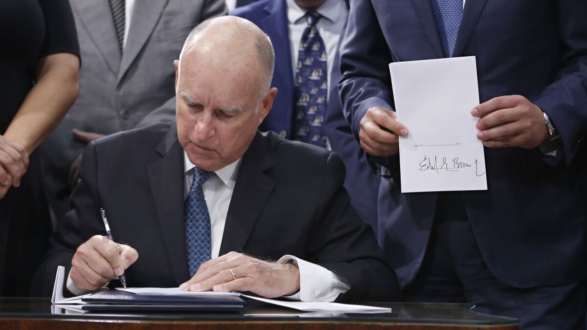 Gov. Jerry Brown signs a copy Senate Bill 100 on Sept. 10 in Sacramento. The legislation sets a goal of phasing out all fossil fuels from the state's electricity sector by 2045.