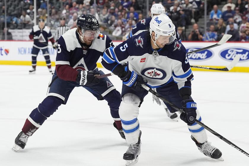 Winnipeg Jets defenseman Brenden Dillon, right, collects the puck as Colorado Avalanche center Yakov Trenin, left, defends in the third period of an NHL hockey game Saturday, April 13, 2024, in Denver. (AP Photo/David Zalubowski)