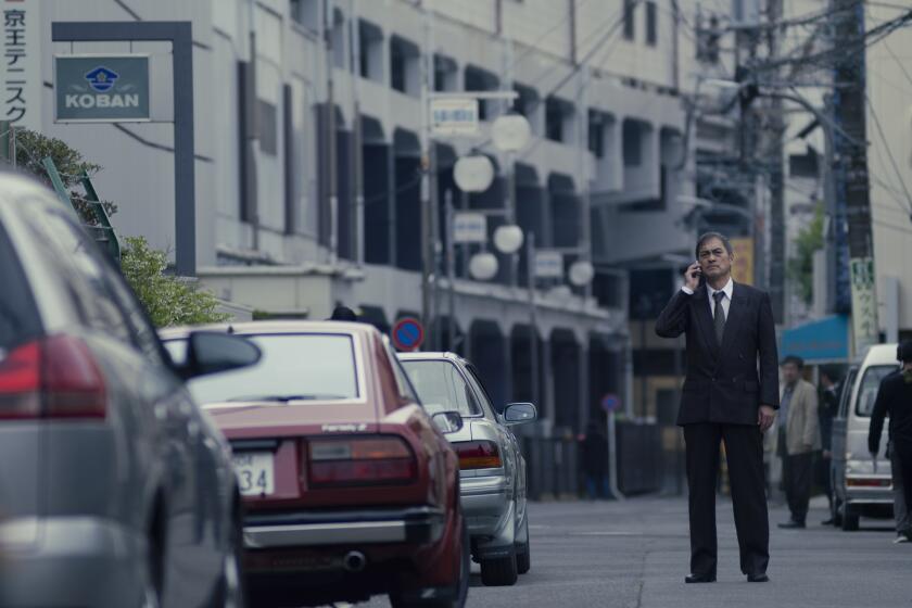 A man stands in the middle of the street in a suit, talking on a cell phone. 