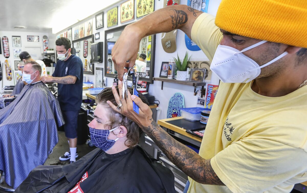 Leucadia Barber Shop manager Emiliano Zermeno (right) cuts the hair of Ben Canedy, 13, on Wednesday, the first day salons were allowed to reopen since the shutdown began in March.