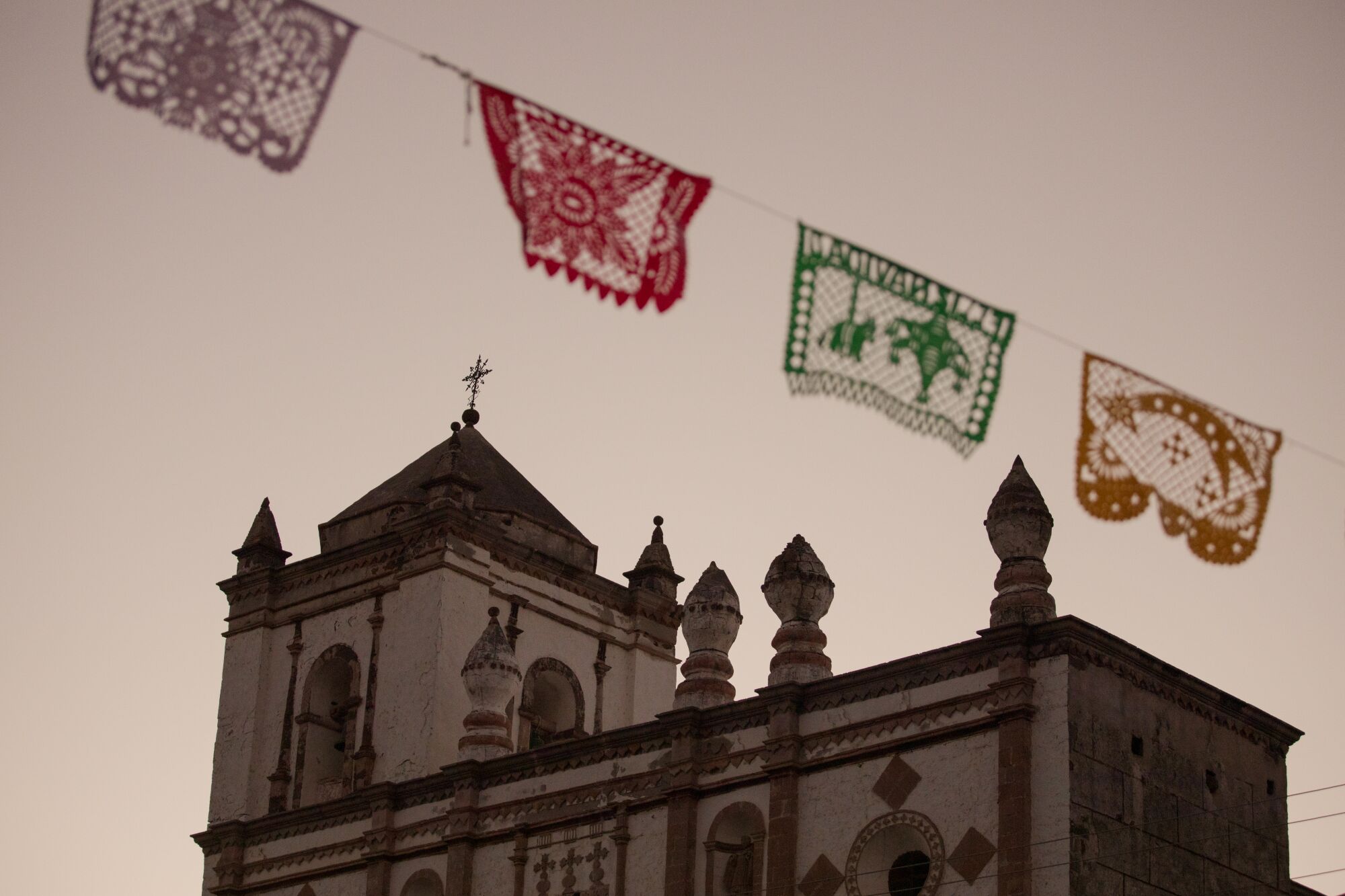 A low-angle view of an ornate church building, with a banner of colorful flags in the foreground.