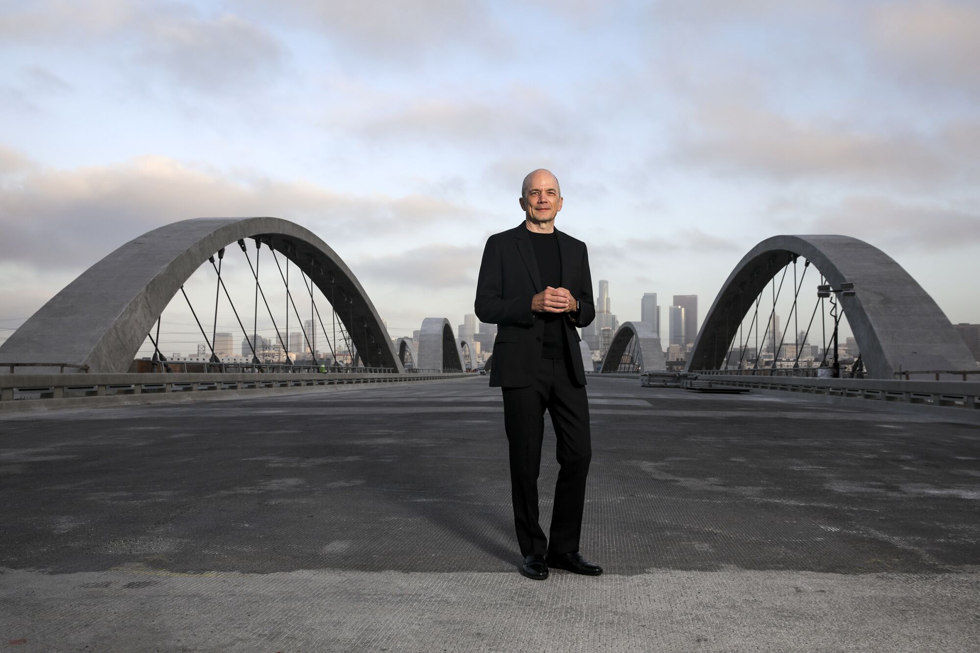 Michael Maltzan, in a suit, stands on the deck of the under-construction 6 Street Viaduct in Los Angeles