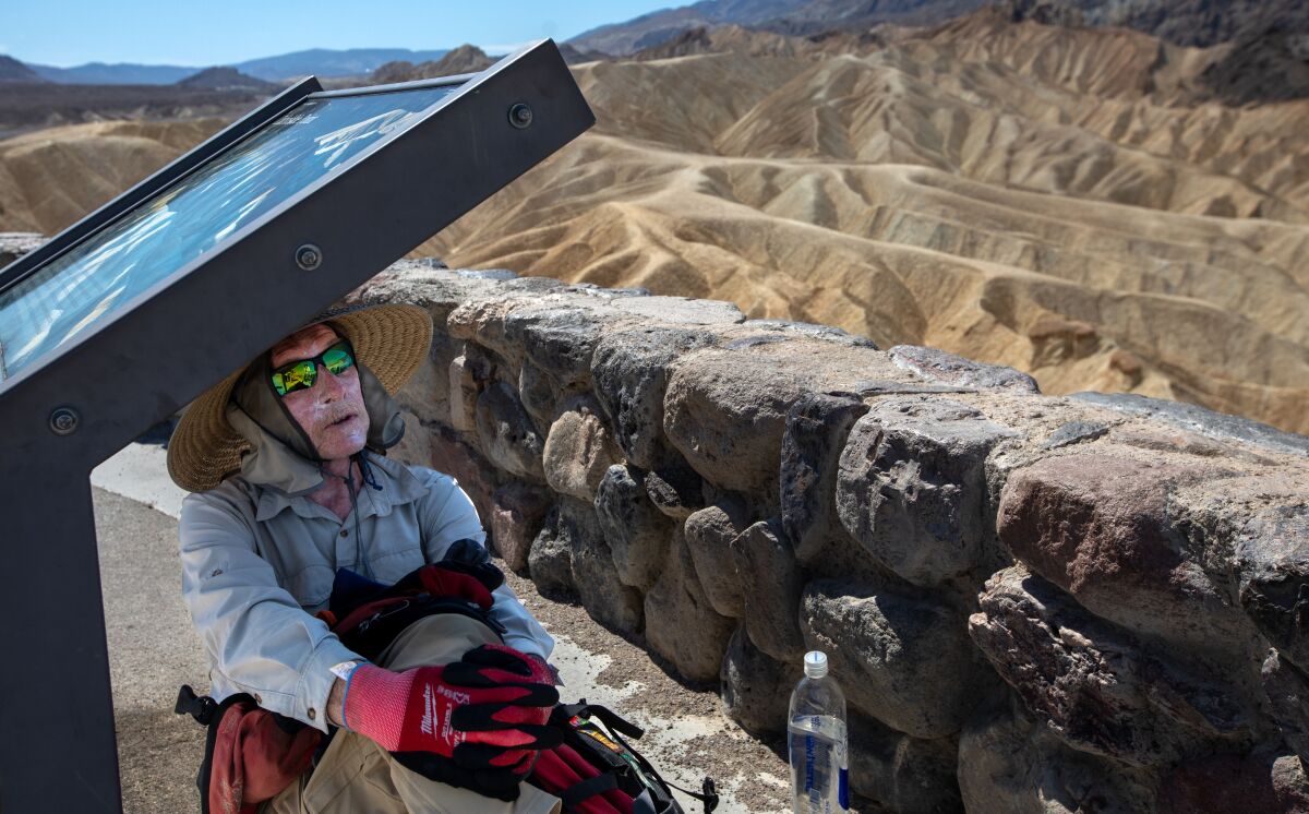 A man sits in the shade of a metal display