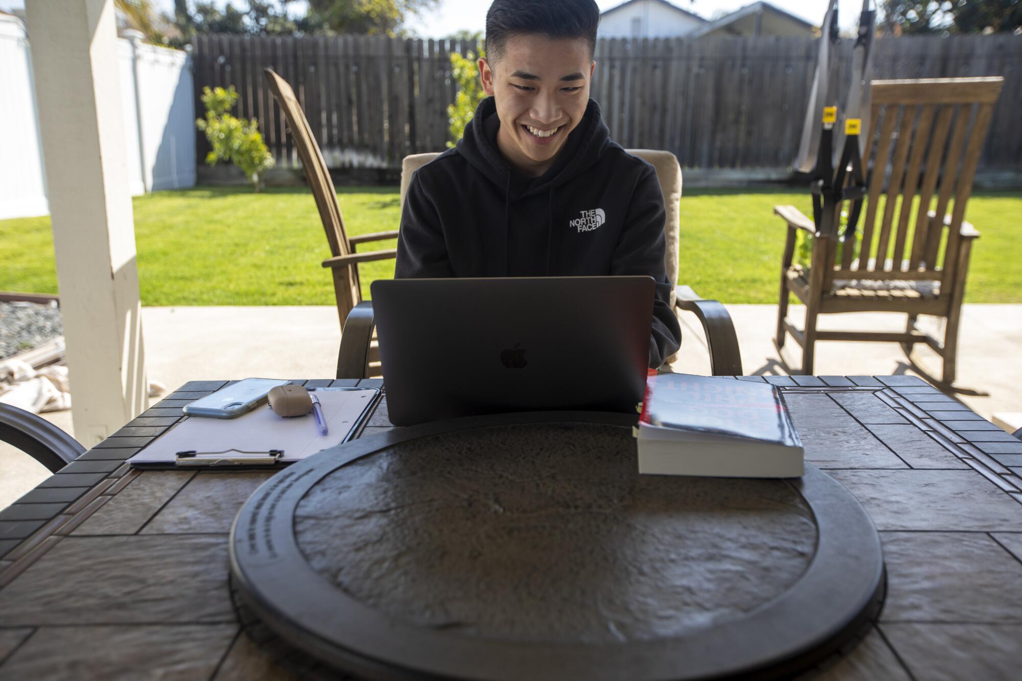 Ryan Fung smiles at his laptop as he sits on a patio