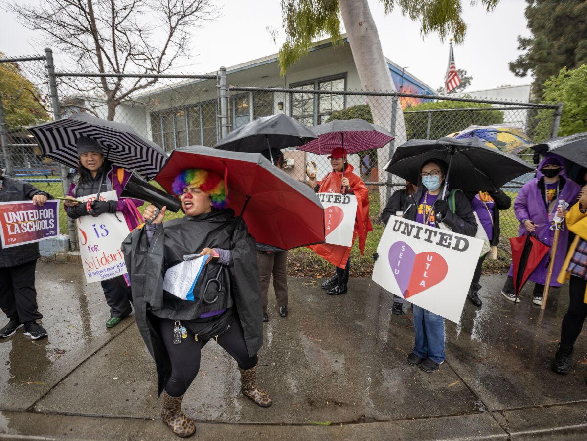 Strikers with umbrellas hold signs on a damp sidewalk.