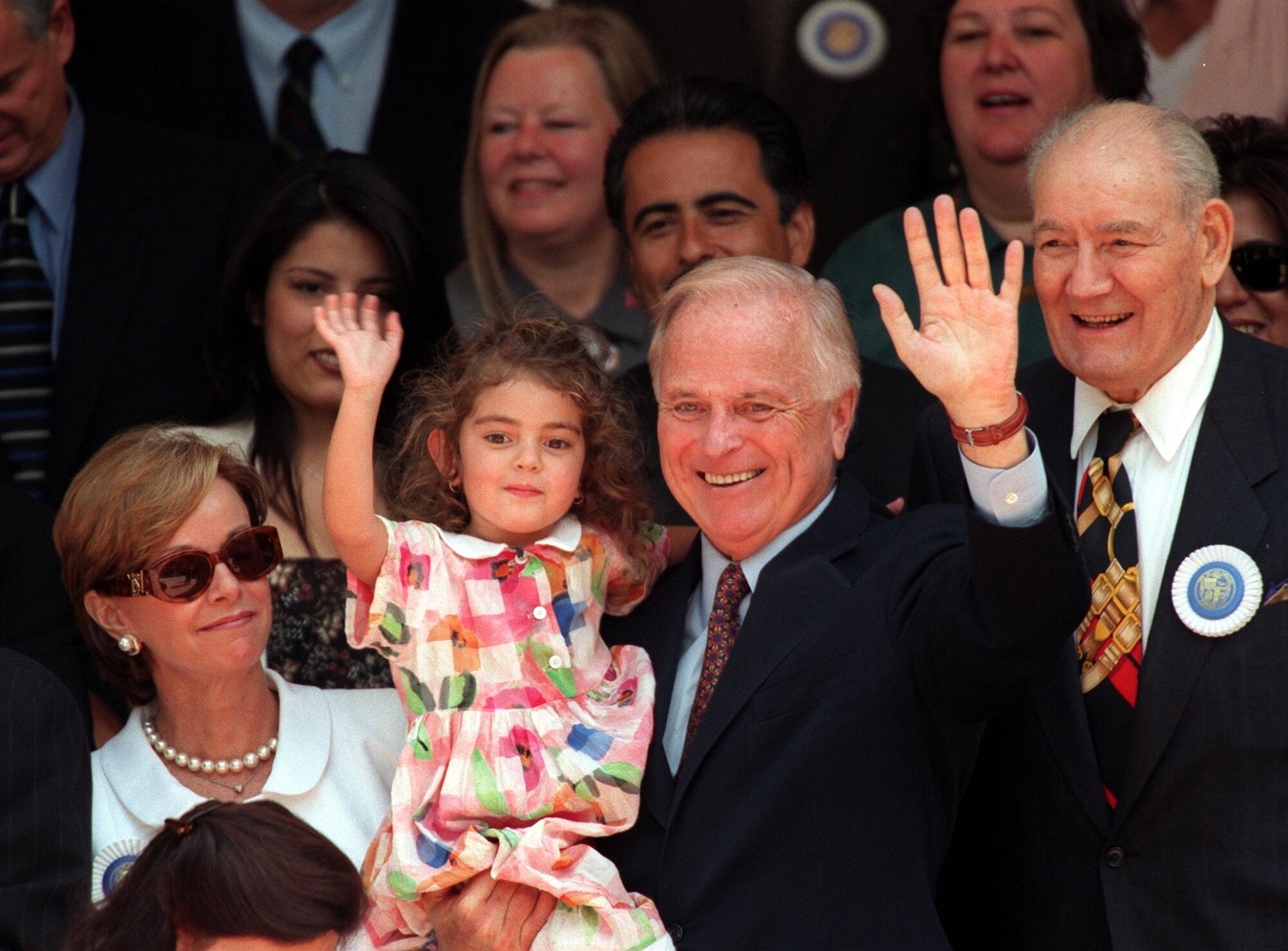 Mayor Richard Riordan, standing in a crowd while holding his granddaughter Nicole Farrel, then 3, waves to well wishers