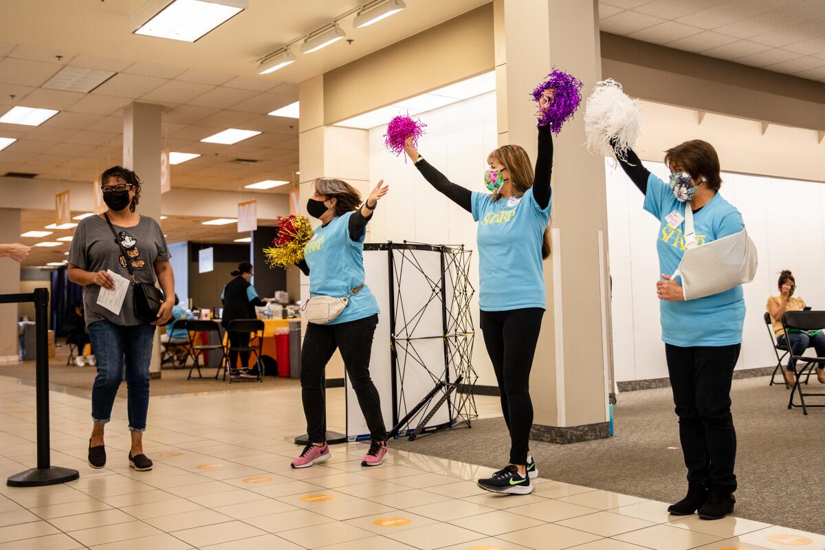 Volunteers Michelle Adams, Terry Castillo, and Helen Vistro cheer for a person who received a COVID-19 vaccination