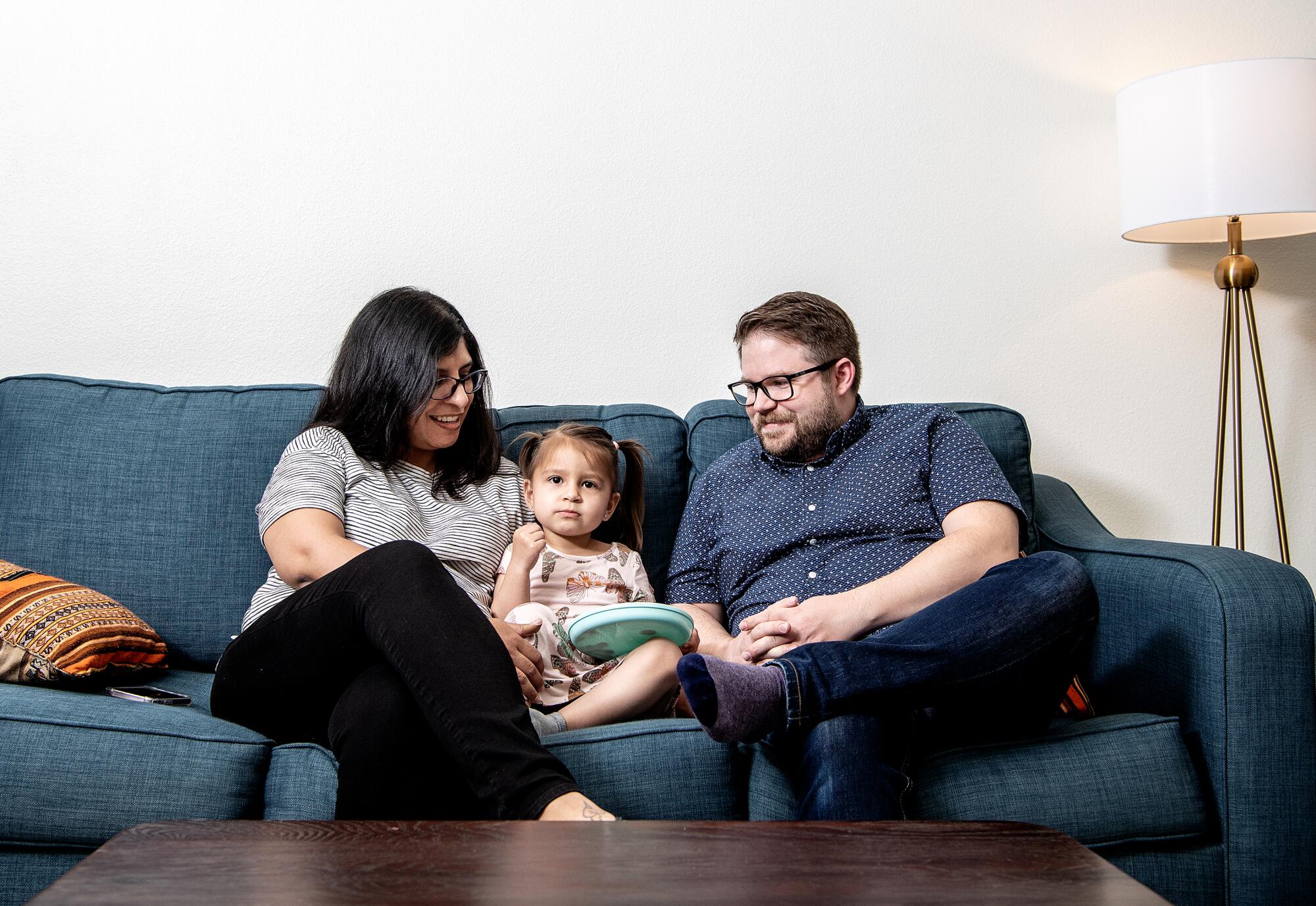 Two parents sit with their daughter on a couch inside the family's condo in Highland Park.