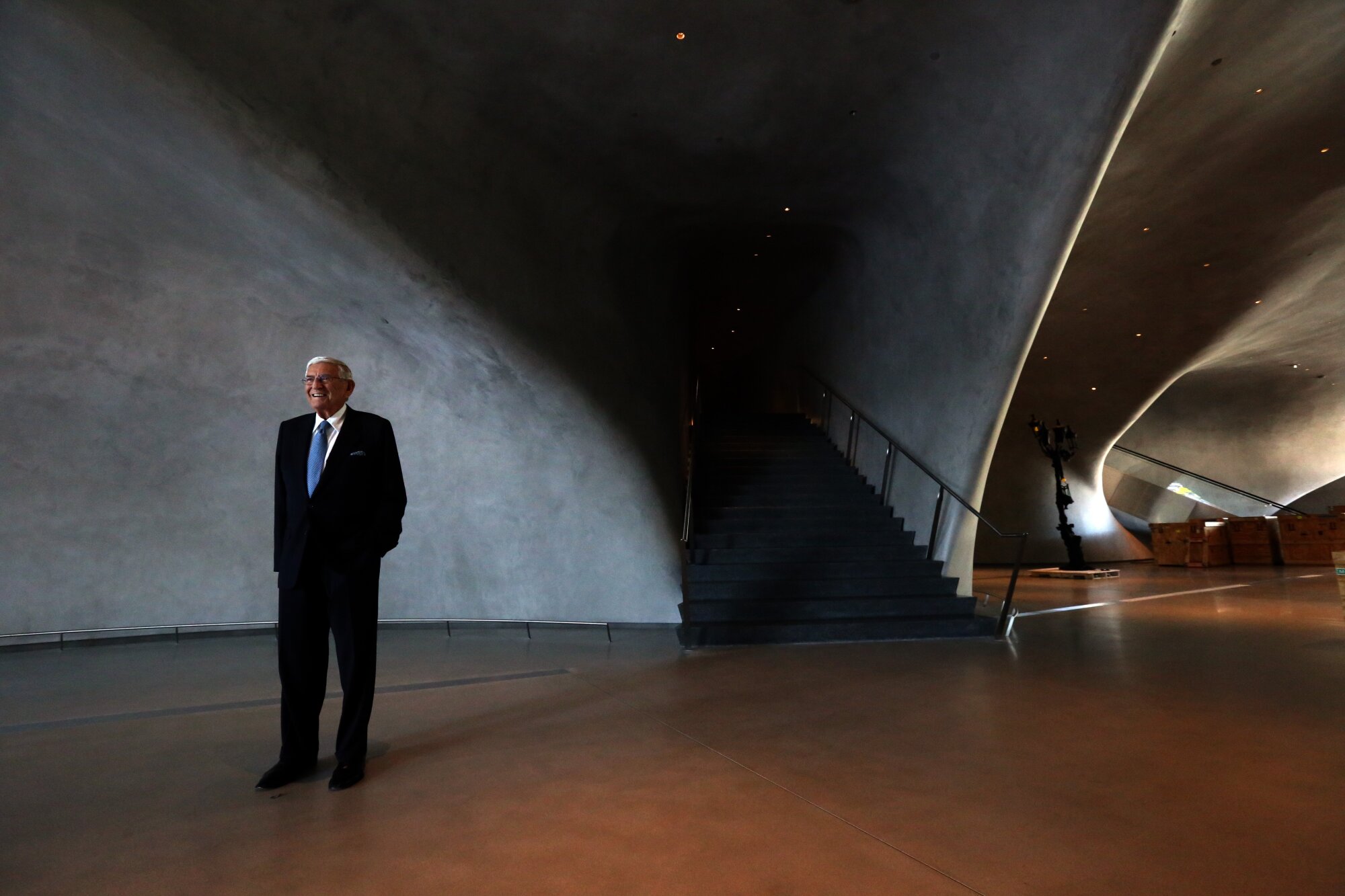 Eli Broad poses for a photo in a cavernous space with curved, shaded walls.