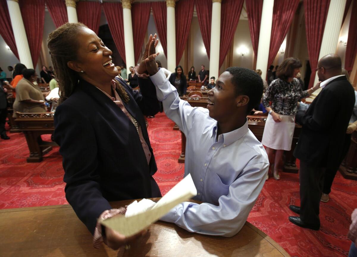 Sen. Holly Mitchell (D-Los Angeles)is the only African American in the state Senate after Sen. Roderick Wright took a leave of absence. Above, Mitchell gets a high-five from her son, Ryan, 13, after signing her oath of office at the Capitol last fall.