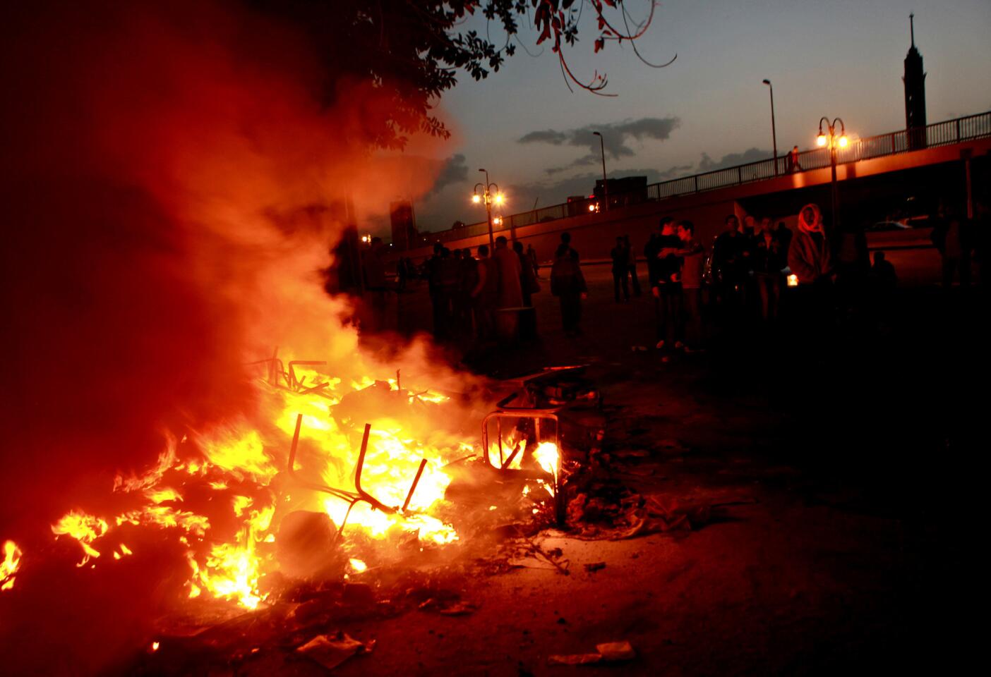 Men add fuel to the fire burning in front of ruling party headquarters in Tahrir Square, where protests continued into the night.