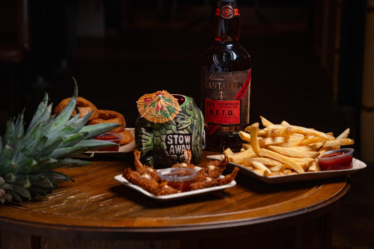 A spread with coconut shrimp, French fries, onion rings, a tiki-style mug and bottle of rum.